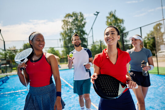Multiracial group of happy friends leaving sports court after playing paddle tennis.