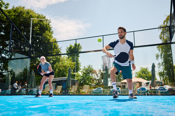 Male athlete plays mixed doubles on paddle tennis court.