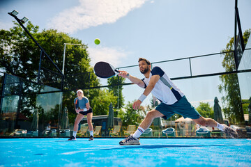 Paddle tennis player making an effort to while hitting ball during match on outdoor court.