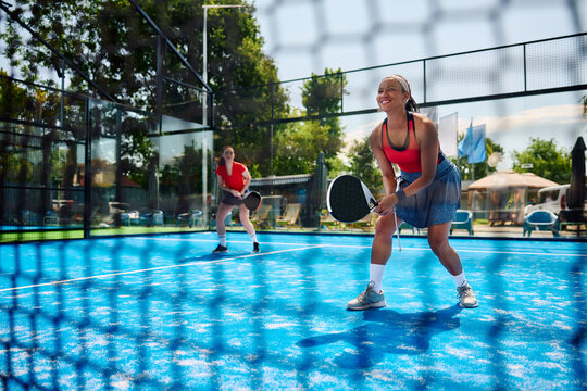 Black female paddle tennis player plays doubles on outdoors court.