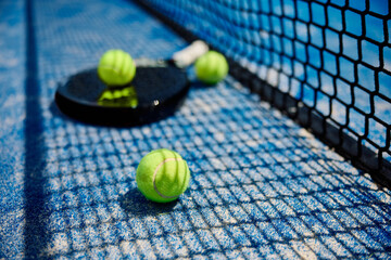 Yellow balls and racket on paddle tennis court.