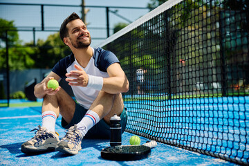 Happy paddle tennis player relaxing on sports court and looking away.