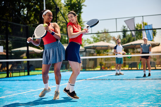Happy female mixed doubles partners celebrate during paddle tennis match.