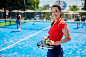 Happy athletic woman playing doubles in paddle tennis and looking at camera.