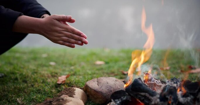 Bonfire, wood and camping with warm hands, heat and relax in nature, grass and rocks for safety at bbq. Fire, flames and burning for charcoal, barbecue and person for adventure, camp and survival