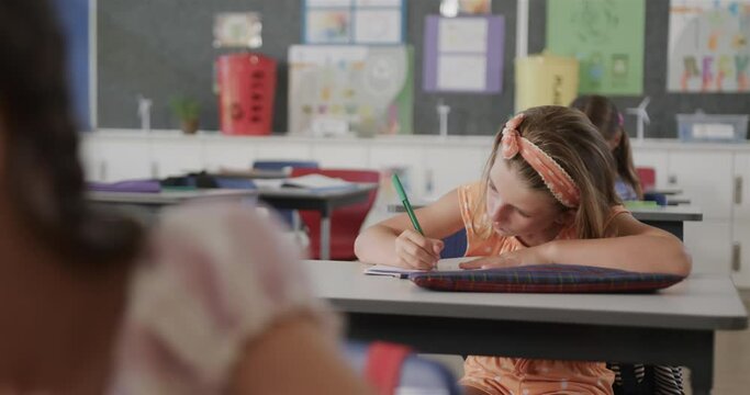 Focused diverse schoolgirls writing at desks in elementary school class, slow motion