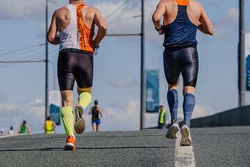 rear view two male athlete in compression socks running marathon race on road, summer sports event