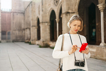 Young blond woman tourist visiting European city, looking for information on cell phone app 