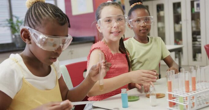 Happy diverse schoolgirls doing experiments in elementary school chemistry class, slow motion