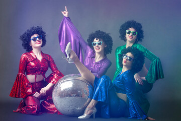 Music or dance group of girls in disco style posing on a gray background with a disco ball. The...