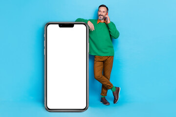 Full body photo of mature handsome man talking phone lean on vertical panel dressed stylish green outfit isolated on blue color background