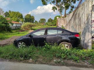 A black car lies abandoned in the bushes, a silent witness of a mysterious accident. The car is badly damaged, with dents, scratches and rusty. 