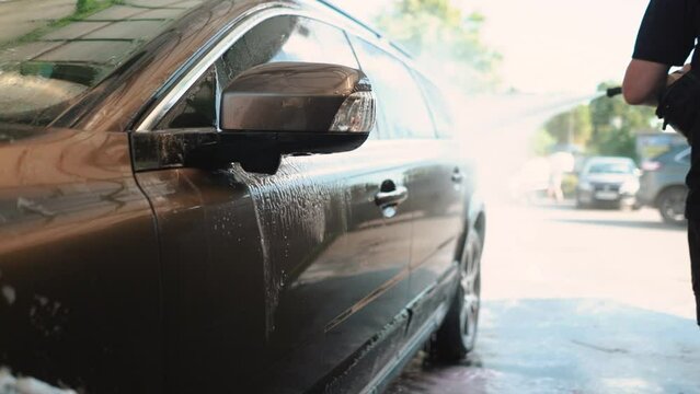 A male driver washes his car with water and wax at a self-service car wash in the summer