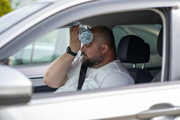 Exhausted overweight man driver suffering from heat inside car with broken air conditioner touch bottle of water to forehead closed eyes try cool. Male feel sick headache from hot air temperature 