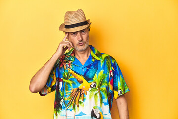 Middle-aged man in Hawaiian shirt and straw hat Middle-aged man in Hawaiian shirt and straw hatpointing temple with finger, thinking, focused on a task. © Asier