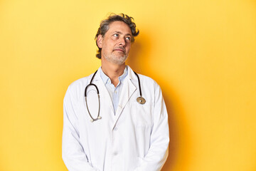 Middle-aged doctor standing against a yellow backdrop dreaming of achieving goals and purposes