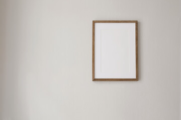 Vertical wooden picture frame mockup hanging on beige wall. Poster mock-upframe on pastel background in sunlight. Home interior with soft shadow, empty copyspace. Art display concept. Minimal interior