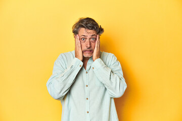 Middle-aged man posing on a yellow backdrop whining and crying disconsolately.