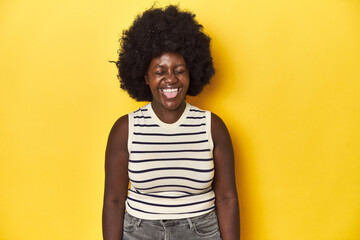 Fototapeta na wymiar African-American woman with afro, studio yellow background funny and friendly sticking out tongue.