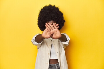 African-American woman with afro, studio yellow background doing a denial gesture