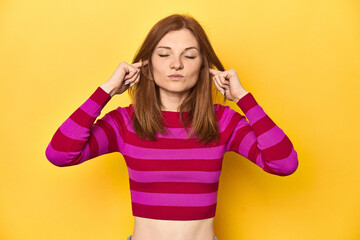 Fototapeta premium Redhead in pink-red striped shirt, casual look covering ears with fingers, stressed and desperate by a loudly ambient.
