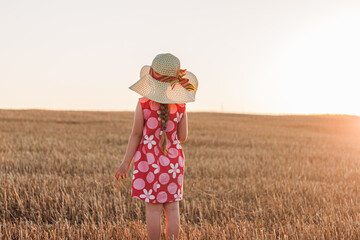 Child girl in straw hat summer dress in wheat spikelets field back view Smiling kid on sunset countryside landscape. Family farming agriculture environment ecology concept. Cottagecore style aesthetic