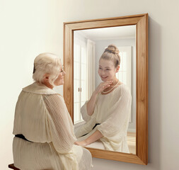 Creative conceptual collage. Smiling senior woman looking in mirror and remembering her past. Young...