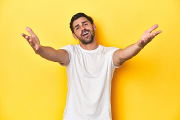 Fototapeta premium Caucasian man in white t-shirt on yellow studio background feels confident giving a hug to the camera.