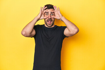 Caucasian man in black t-shirt, yellow studio backdrop keeping eyes opened to find a success opportunity.