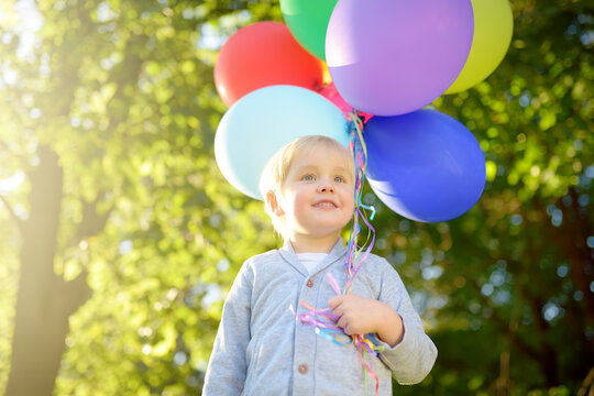 Cute little child going to congratulate a friend on his birthday. Toddler holding bundle of colorful balloons and gift in a festive box. Anticipation of the holiday.