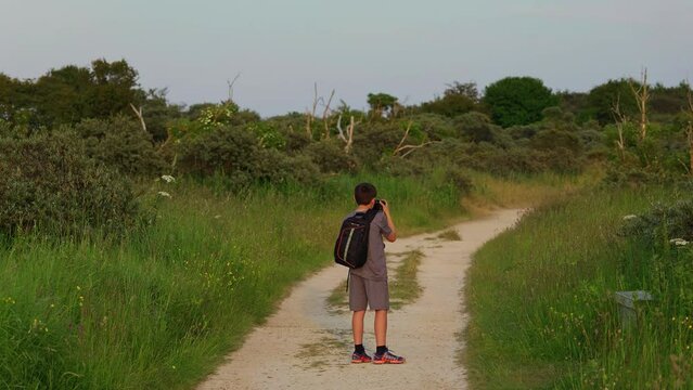 Young boy photographer, holding camera and taking pictures of country wildlife and landscapes in the UK