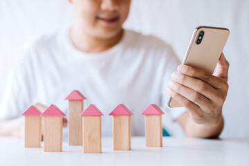 young man putting a triangle wooden block to show the construction of a wooden in the shape of a house, insurance business, real estate agent build a home concept.search data from smartphone