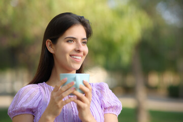 Happy female holding coffee cup standing in a park