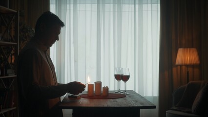 The man is getting ready for a date. The dark silhouette of a man lights candles with matches....