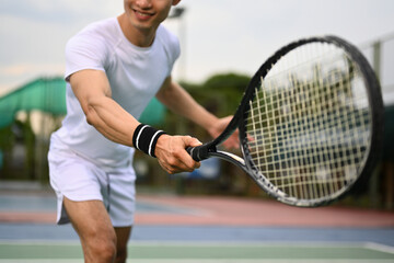 Smiling muscular man hitting ball with racket to return ball over net. Sport, fitness, training and active life concept