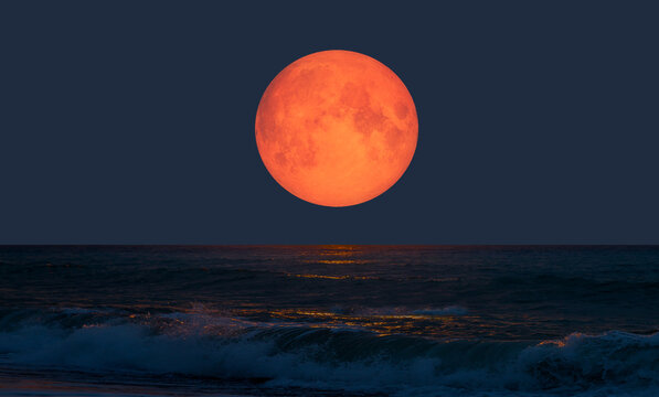 Night sky with orange moon in the clouds over the calm blue sea "Elements of this image furnished by NASA"