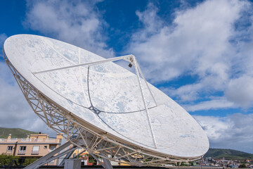 View of a large satellite dish to observe the cosmos, decorated with the lunar topography, with large white clouds in the background.