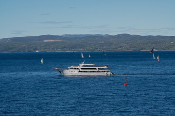A large cruise ship leaves the port. There are a lot of sailing ships and yachts in the sea.
