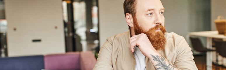 portrait of thoughtful, bearded and tattooed entrepreneur looking away in modern office environment, professional headshot,  business lifestyle concept, banner with copy space