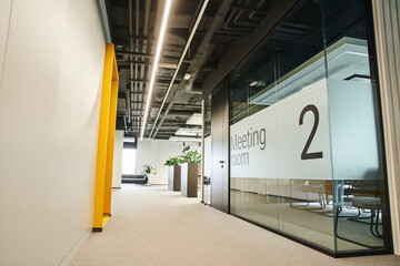 long and wide corridor with led lighting, green plants, meeting room behind glass transparent wall...