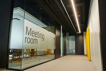 meeting room behind transparent glass wall, long and wide corridor with led lighting in...