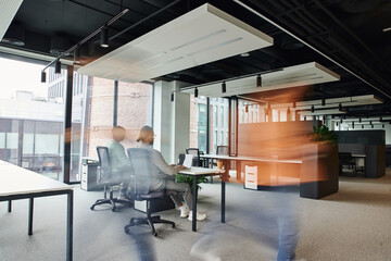 motion blur of man walking near business people working in open space office environment with high...