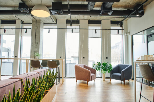 cozy waiting lounge with large windows, soft and comfortable armchairs, green and natural plants in modern coworking environment, workspace organization concept