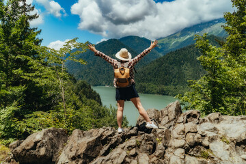 Hiking traveller woman with backpack hands up enjoying beautiful view of turquois blue Lake Ritsa in Abkhazia