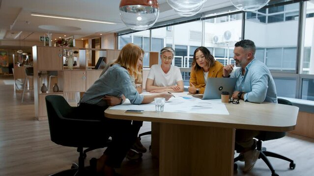 Architectural designers having a team meeting in an office, discussing blueprints and plans for a project. Group of business people contributing ideas as they collaborate on a design.