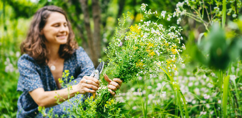 Young cheerful smiling woman in a summer dress picking a bouquet of wild flowers in a summer garden