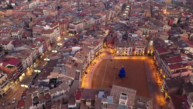 Aerial view of Spanish town of Vic overlooking central square decorated with festive lighting and main Christmas tree on eve of holidays in winter evening . High quality 4k footage
