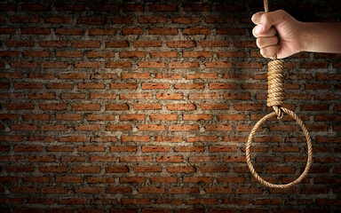 Hand holding rope noose with hangman's knot hanging on dark brick wall