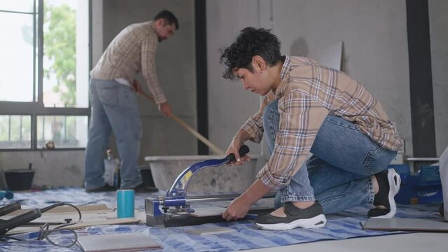 Asian artisan tiler at construction site, asia Workman cutting ceramic tiles with handy machine at the construction site indoors