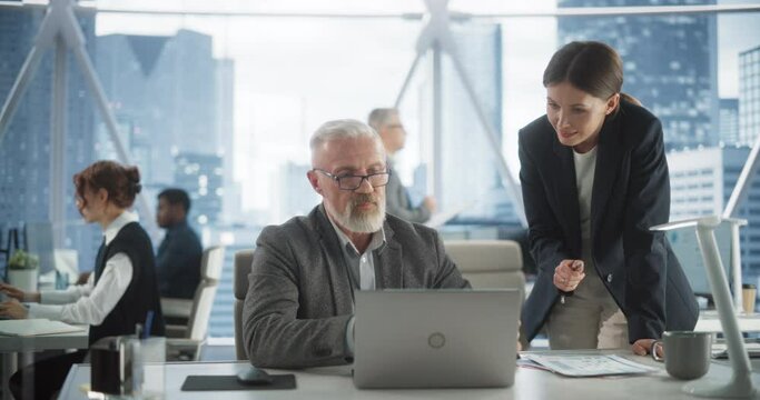 Senior Male Financial Analyst And Female Project Manager Working With Laptop Computer In Modern Downtown Office. Caucasian Man And Woman Looking For Investment Opportunities In Banking or Tech Sectors